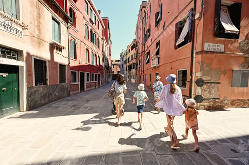 Preview: Back of family tourists walk in Ramo De La Piscina street, Venice, Italy.