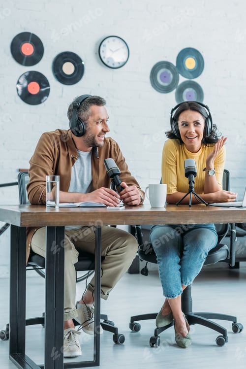 Preview: two smiling radio hosts sitting at workplace in broadcasting studio and recording podcast together