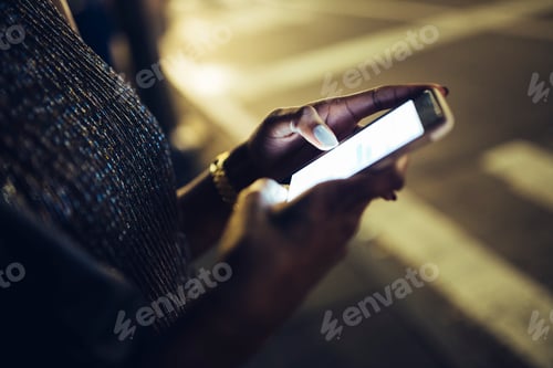 Preview: Hands of woman holding smartphone at night, close-up