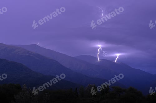 Preview: Sudden flash of lightning striking the peak of a mountain under a purple sky covered by foggy clouds