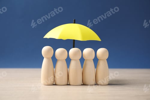 Preview: Human figures under umbrella on light wooden table against blue background. Insurance concept