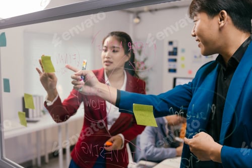 Preview: Two asian businesspeople are analyzing diagrams and flowcharts drawn on a glass board with sticky no