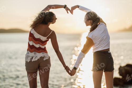 Preview: Two Women Making A Heart Shape With Their Hands And Enjoying Sunset At The Beach