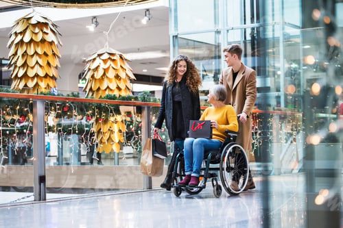 Preview: A grandmother in wheelchair and teenage grandchildren in shopping center at Christmas.