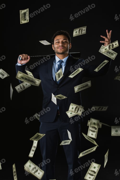 Preview: Confident young businessman holding baseball bat and dollar banknotes falling on black