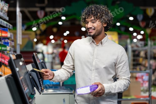 Preview: A man smiles while paying with a credit card at a supermarket self-checkout.