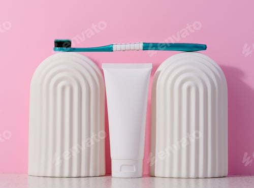 Preview: White plastic toothpaste tube and toothbrush on a pink background.