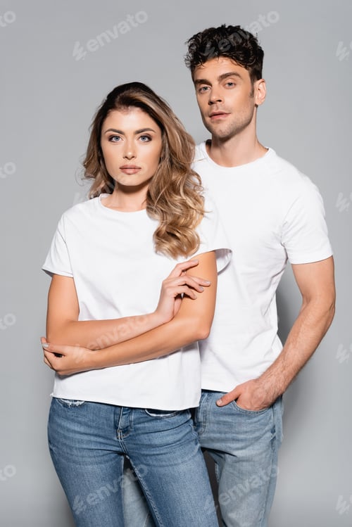 Preview: young couple in white t-shirts and jeans posing isolated on grey