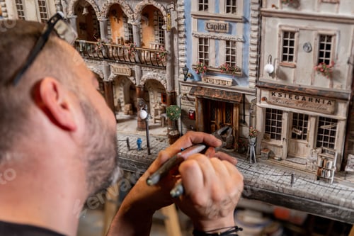 Preview: Modeller man working at scale model of miniature building in his workshop full of tools