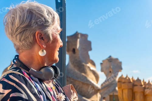 Preview: Senior tourist woman wearing headphones exploring park guell in barcelona, catalonia, spain