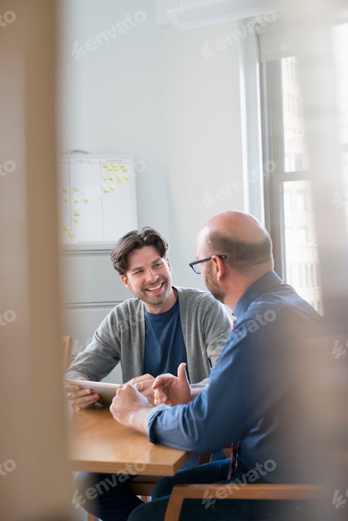 Preview: Two business colleagues in an office talking and referring to a digital tablet.
