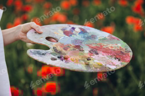 Preview: Painter holding palette with colorful oil paint in poppy field