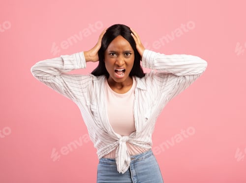 Preview: Furious black woman screaming and holding her head on pink studio background