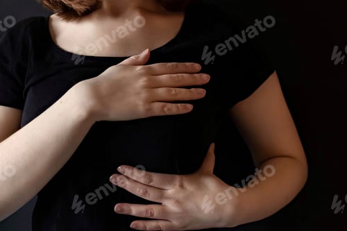 Preview: A girl in a black t-shirt clasps her chest with both hands. The concept of breast cancer.