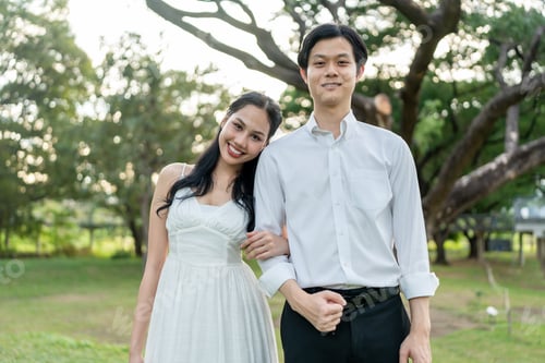 Preview: Portrait of Asian married couple looking at camera in park during sunset.