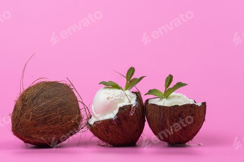 Preview: Vanilla ice cream balls in fresh coconut halves decorated with mint leaves on a pink background