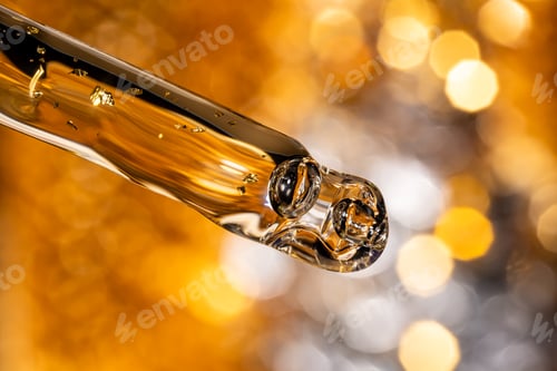 Preview: Liquid serum and dropper on a bokeh golden background macro. 24k gold Serum drop