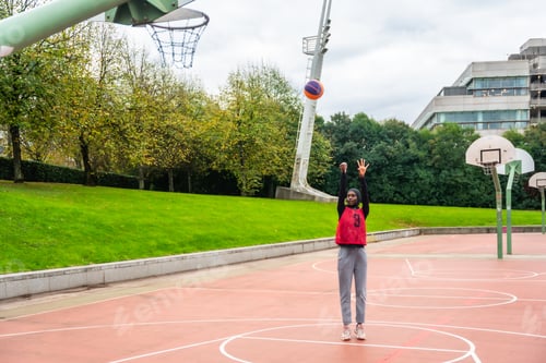 Preview: Muslim woman wearing hijab playing basketball, shooting ball outdoors