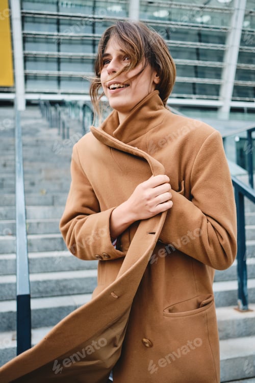 Preview: Young attractive woman fastening up coat from cold happily walking outdoor