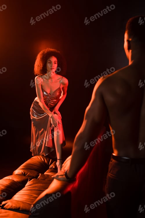 Preview: elegant african american woman in dress looking at shirtless man on blurred foreground