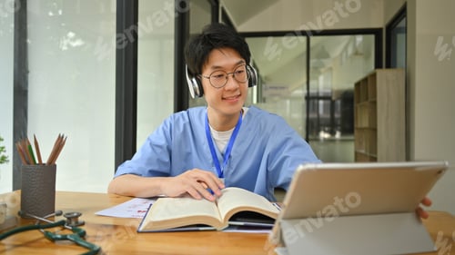 Preview: Young male medical students wearing headphone and using digital tablet in library.