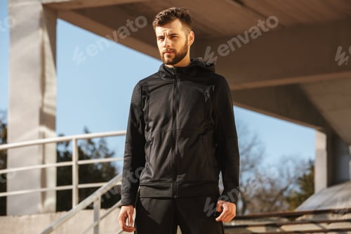 Preview: Portrait of a confident young sportsman in earphones standing