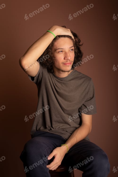 Preview: Caucasian male sitting on a chair styling his hair on a brown background