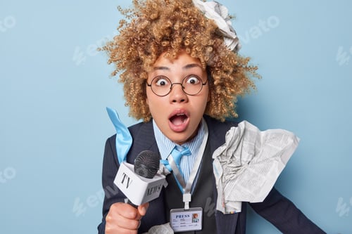 Preview: Shocked curly female TV reporter makes reportage stares stunned with widely opened mouth holds micro