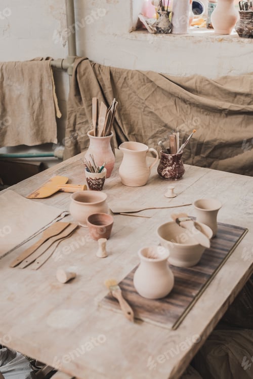 Preview: high angle view of handmade clay pots near equipment on wooden table in pottery