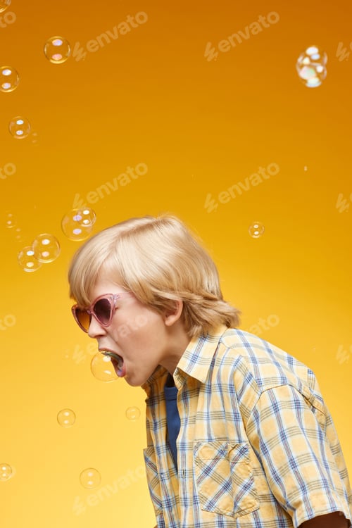 Preview: Preteen Boy in Sunglasses Catching Soap Bubbles with Mouth in Studio