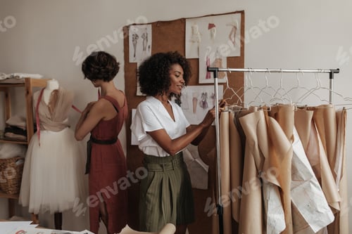 Preview: Beautiful stylish young women in trendy outfits design new clothes. Attractive ladies work in offic