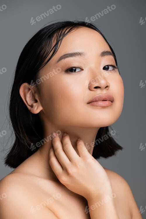 Preview: portrait of asian woman with bare shoulders and natural makeup touching neck and looking at camera