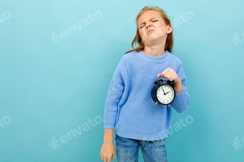 Preview: european girl holding an alarm clock on a light blue background