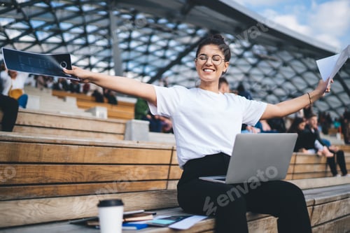 Preview: Happy Caucasian student rejoicing in public place using netbook and papers for planning