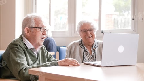 Preview: Happy senior couple chatting online using laptop at nursing home
