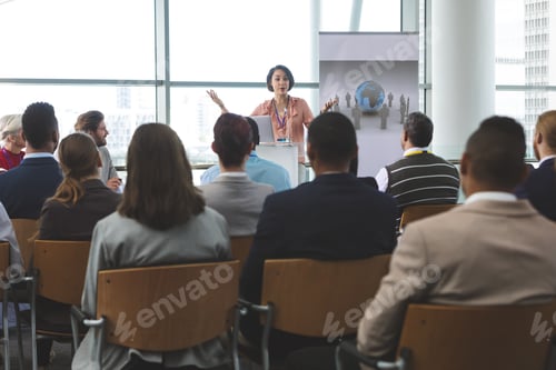 Preview: Businesswoman speaking animatedly to crowd of business people at business seminar in office