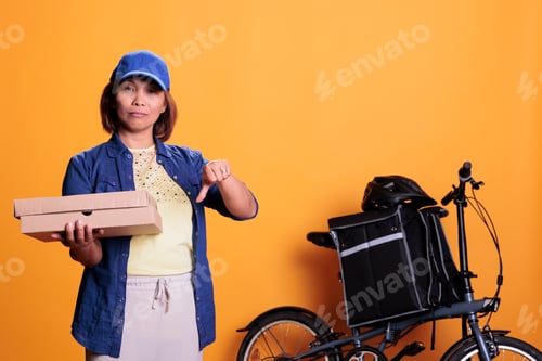 Preview: Asian pizzeria delivery worker doing thumbs down, gesture while holding carton cardboard