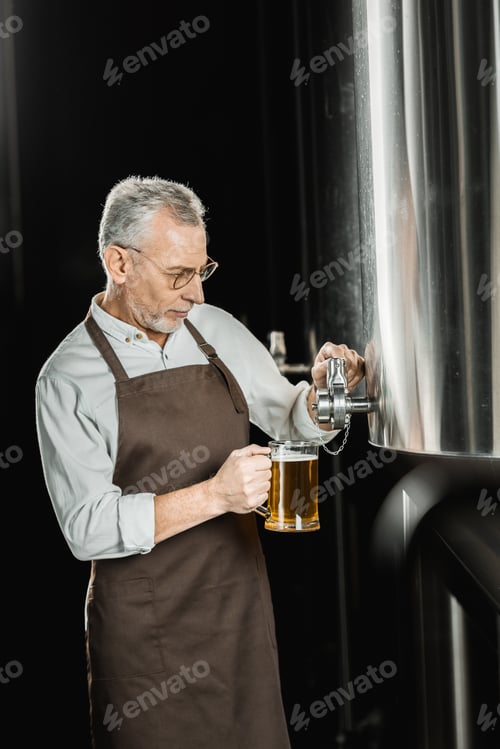 Preview: handsome senior brewer pouring beer for testing in brewery