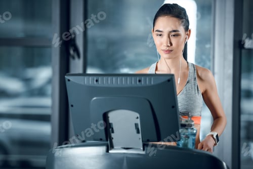 Preview: young attractive sportswoman jogging on treadmill at gym and looking at screen