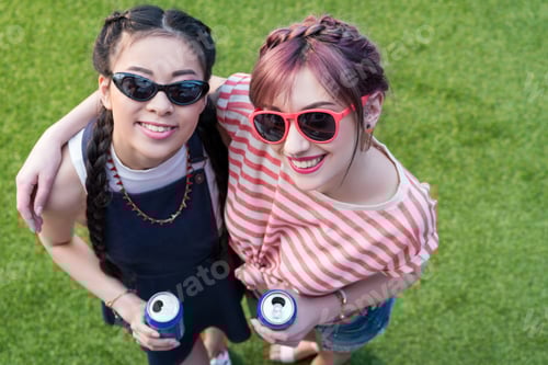 Preview: high angle view of young multiethnic women in sunglasses holding soda cans and smiling at camera