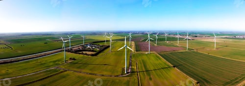 Preview: Panoramic view of windmills in a green cultivated fields on a sunny day