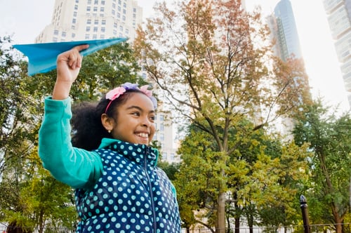 Preview: Girl throwing paper airplane smiling, New York, USA