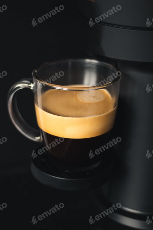Preview: Close up shot of a cup of coffee in a black espresso machine isolated on a dark background