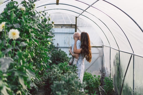 Preview: Woman playing with her child in a greenhouse with flowers. Happy Mother's Day