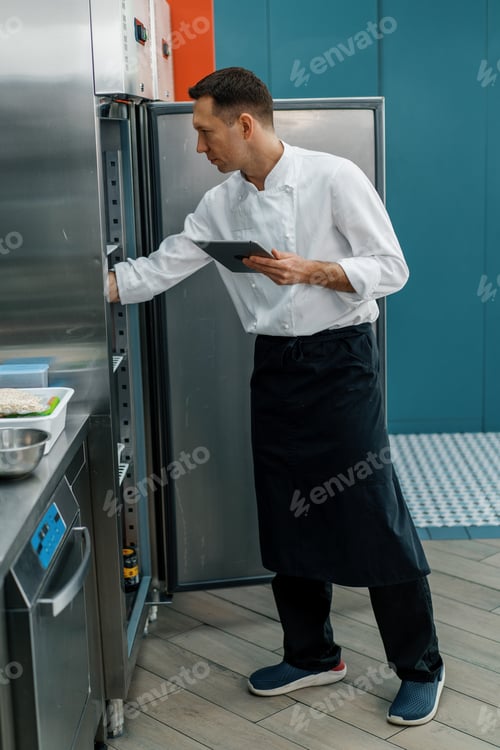 Preview: Professional chef using tablet computer for recipes while working in modern kitchen cooking concept