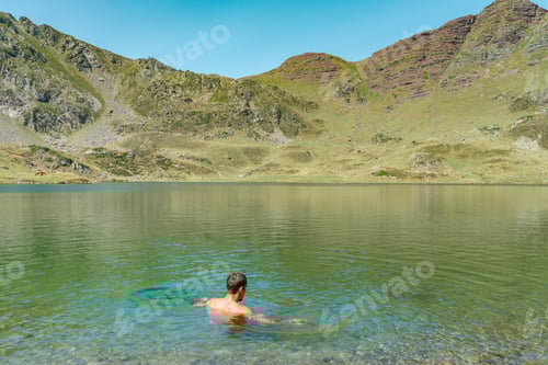 Preview: Young man swimming in turquoise blue crystal clear water in the wild lake summer vacation relaxing