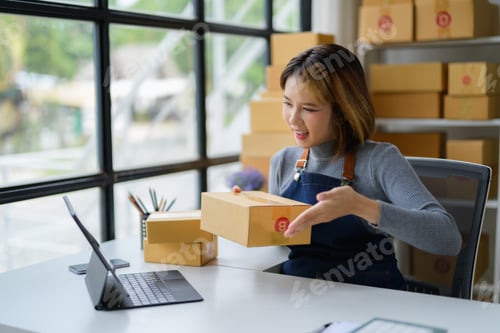 Preview: Asian Female Seller Showing Parcel Packaging to Tablet in Warehouse Storage Room