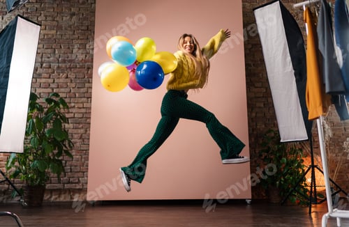 Preview: Fashion studio portrait of a happy young woman with balloons jumping, backstage of photoshooting .