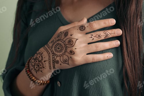 Preview: Woman with beautiful henna tattoo on hand against green background, closeup. Traditional mehndi