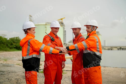 Preview: Team building event among construction workers in safety gear near coastal area during overcast day